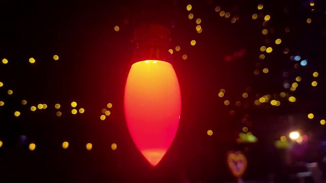 A red C7 Christmas light bulb glows brightly, surrounded by a soft bokeh of yellow fairy lights, creating a festive atmosphere.