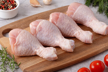 Fresh chicken drumsticks and vegetables on a cutting board in a kitchen setting ready for cooking