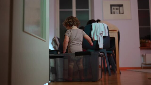 Toddler standing inside transparent storage box then spinning and falling down, playful childhood moment of simple home fun and carefree exploration