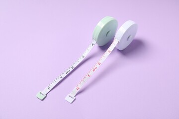 Measuring tapes on violet background, closeup view