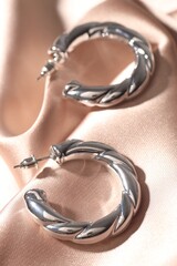Shiny silver earrings on pink silk cloth, closeup