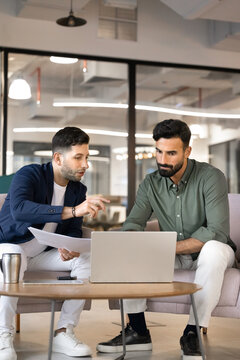 Two serious Middle Eastern male colleagues collaborating on project, reviewing data, working on presentation on laptop, discuss strategy, making business decisions during meeting in corporate office