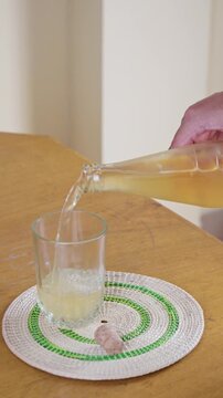 Hand pouring amber kombucha fermented probiotic beverage from clear glass bottle into drinking glass
