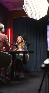 Podcast host interviews social media influencer seated at table with microphones during live streaming, discussing digital trends, online branding, personal experience in professional recording studio