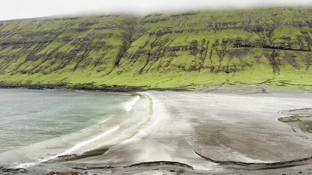Green nordic landscapes of the Faroe Islands. The picturesque black sand beach under green slopes near Sandvik village, Suduroy island.