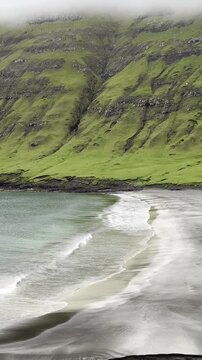 Green nordic landscapes of the Faroe Islands. The picturesque black sand beach under green slopes near Sandvik village, Suduroy island.
