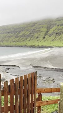Green nordic landscapes of the Faroe Islands. The picturesque black sand beach under green slopes near Sandvik village, Suduroy island.