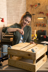 Woman assembling wooden crate furniture with a screwdriver in workshop