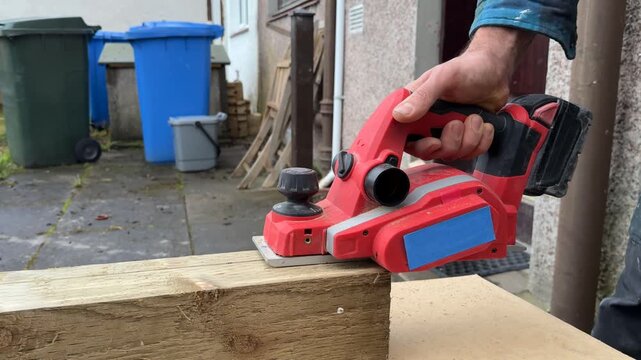 An electric planer cutting a board. A close-up side view. A craftsman using an electric planer. Interior renovation. Interior restoration and refurbishment. Home improvement.