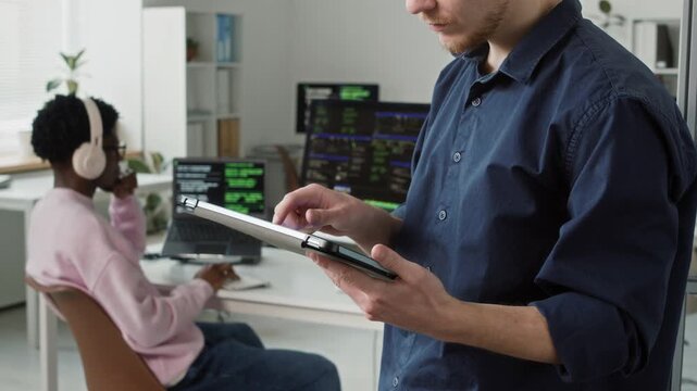 Cropped shot of young adult male IT programmer tapping on digital tablet screen testing app performance in shared office space