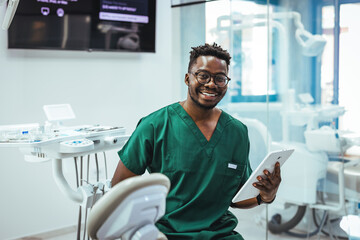 Smiling Dentist in Green Scrubs Holding Tablet in Modern Dental Clinic