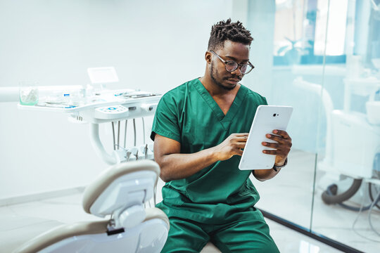 Dentist in Green Scrubs Using Tablet in Modern Dental Clinic Consultation and Record Review