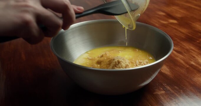 Crushed cookies mixed with melted butter in metal bowl to prepare cheesecake crust. Close up of homemade dessert base preparation on wooden table in kitchen.