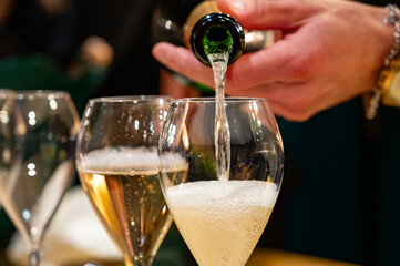 Pouring in glasses of french sparkling wine champagne with little bubbles, tasting wine, celebration, wedding or champagne tour with visit of caves, Reims, France © barmalini