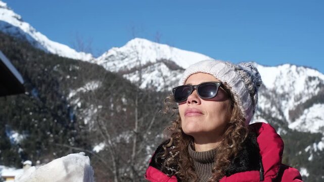 Adult woman blowing snow from her hands in sunny mountain landscape, joyful winter vacation moment with tourist lifestyle, outdoor leisure activity, enjoying nature, freedom, happiness and seasonal tr