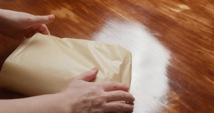 Close-up of a woman wrapping a salmon fillet seasoned with salt and pepper in parchment paper for curing. Homemade salmon preparation in a kitchen, traditional food preservation and home cooking