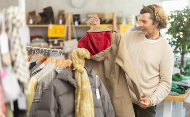 Fototapeta premium Seasonal trade sale, customer review at products in store and pick out clothes. Man search and choose male beige raincoat, purchase some wardrobe items. Style and fashion type look, modern trends.