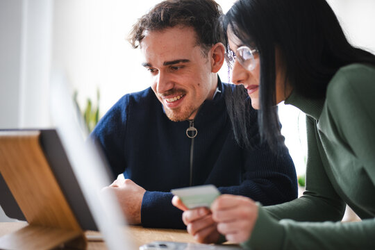 A man and woman are looking at a tablet and holding a card, possibly making a purchase or managing finances together.