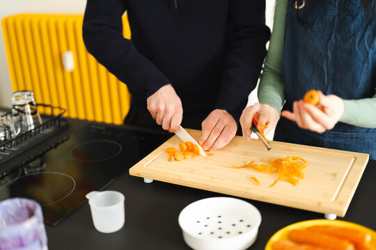 A couple prepares food in the kitchen, one person slices carrots on a cutting board while the other peels a carrot.