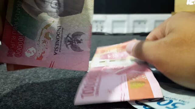 a person counting Indonesian Rupiah banknotes, illustrating concepts related to finance, economy, business transactions, income management, and daily life
