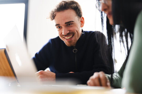 A man and woman collaborate on a project, smiling as they look at a laptop screen together in a bright, modern setting.