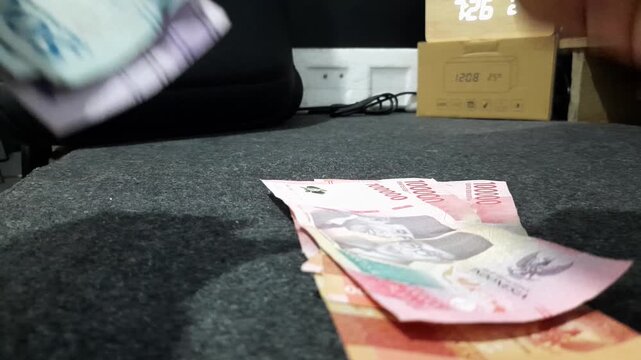 a person counting Indonesian Rupiah banknotes, illustrating concepts related to salary calculation, budgeting, savings, payments, profit, and expense management