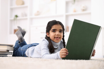Naklejka premium Cute little girl reading book on floor at home
