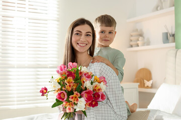 Mother's Day. Happy woman with her son and bouquet of flowers at home