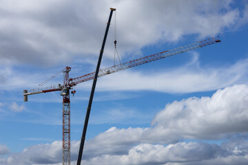 Obraz premium Tower crane and mobile lifting crane working against blue sky with clouds at construction site, showcasing industrial engineering, urban development, heavy machinery operation