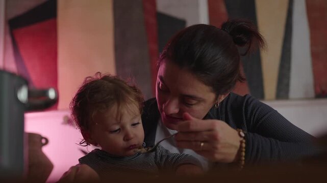 Mother playfully offering spoon to herself before toddler eagerly takes bite, lighthearted family mealtime encouraging cooperation and healthy habits at home
