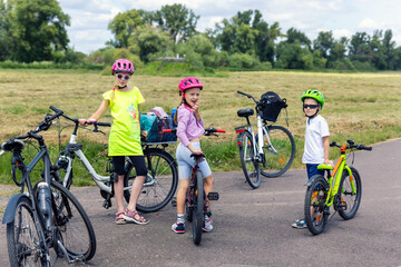 Naklejka premium Children wear helmets stand bicycle rural road summer ride across countryside field green landscape. Friend enjoy cycling adventure freedom outdoor activity healthy lifestyle joyful childhood moment
