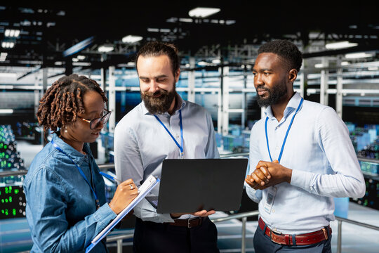 Multiethnic employees team collaborating on maintenance for server rigs and handling AI processing tasks. Data center engineering team supporting machine learning for software development.