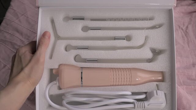 Skincare device kit with multiple attachments displayed in a box on soft pink fabric background. Skincare woman concept. New electric Darsonval