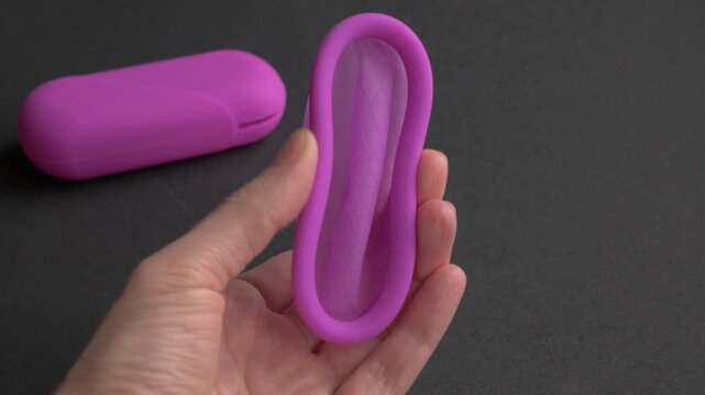 Hand holds silicone menstrual disc, showcasing flexible design and features. Silicone menstrual disc, reusable intimate hygiene. Choice of zero waste eco concept