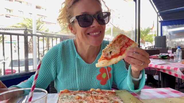 Smiling adult woman eating pizza at restaurant table in daylight, summer tourism scene with relaxed lunch break, enjoying local Italian cuisine, leisure time during vacation and lifestyle dining conce