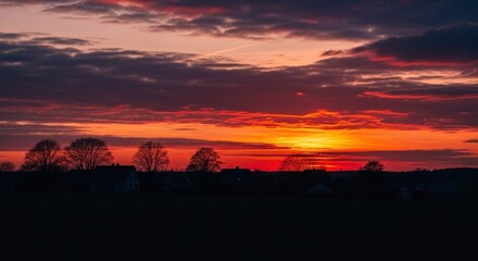 Obraz premium Dramatic sunset over a rural village silhouette, with fiery colors and dark foreground