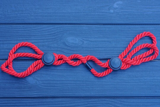 Handcuffs made of red cord with black plastic fasteners lies on a wooden table