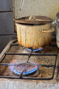 two burners with burning gas flames and a brown dirty pot on a dirty stove in the kitchen