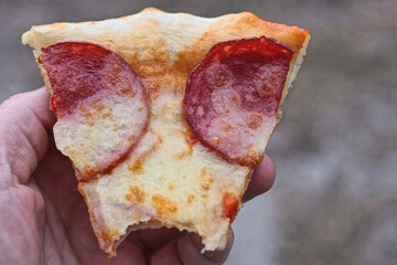hand holding one piece of pepperoni pizza on a gray background outdoors