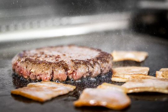 Angus beef burger patty and bacon cooking on griddle
