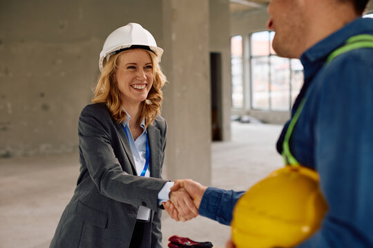 Happy building contractor shaking hand with worker at construction site.