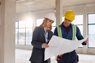 Female project manager and worker analyzing blueprints at construction site.