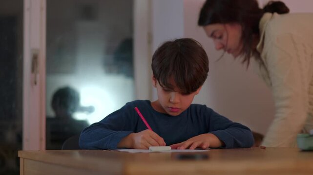 Young boy concentrating on homework at table holding pencil and focusing on school assignment during quiet evening study time at home