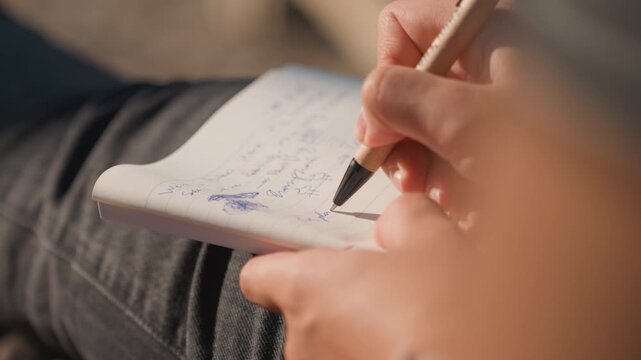 Individual crafting song lyrics on her lap. Creative woman jotting down song ideas in personal notebook. Focused female songwriter sketching lyrics with blue ink on her lap in warm lighting