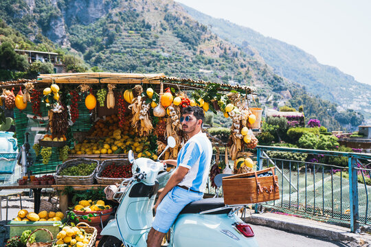Traveler on vintage scooter stopping at colorful fruit stand in Positano Italy