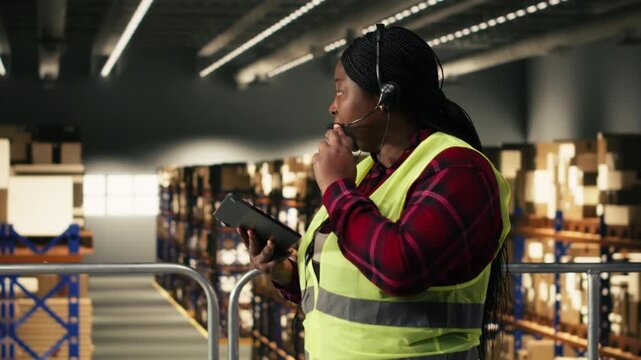 Black female agent assisting customers with package tracking and delivery status, verifying AWB and shipment details on tablet. Managing call center complaints on headset, distribution center.