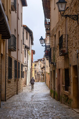 Obraz premium Rear view of a unrecognizable person walking through a narrow medieval street with wet cobblestones in Siguenza Spain featuring historic stone houses with iron balconies and vintage lanterns under a