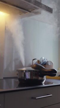 Pressure cooker releasing thick steam on electric stovetop, active kitchen cooking scene, boiling food preparation and intense heat under extractor hood