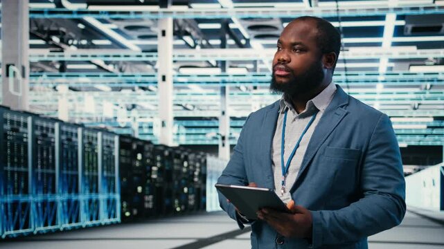 Server room admin using tablet app to enhance operational effectiveness of hardware. African american man in data center using device to monitor infrastructure rackmounts, camera A