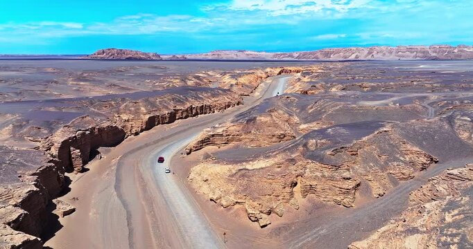 Aerial view of a car driving on a winding road through a deep, dramatic canyon in the remote desert of Xinjiang, China.